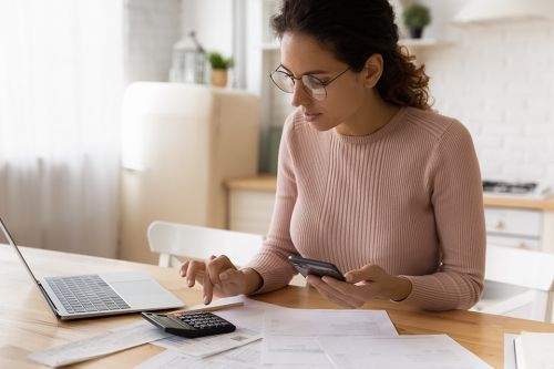 Frau mit Smartphone, Taschenrechner und Laptop